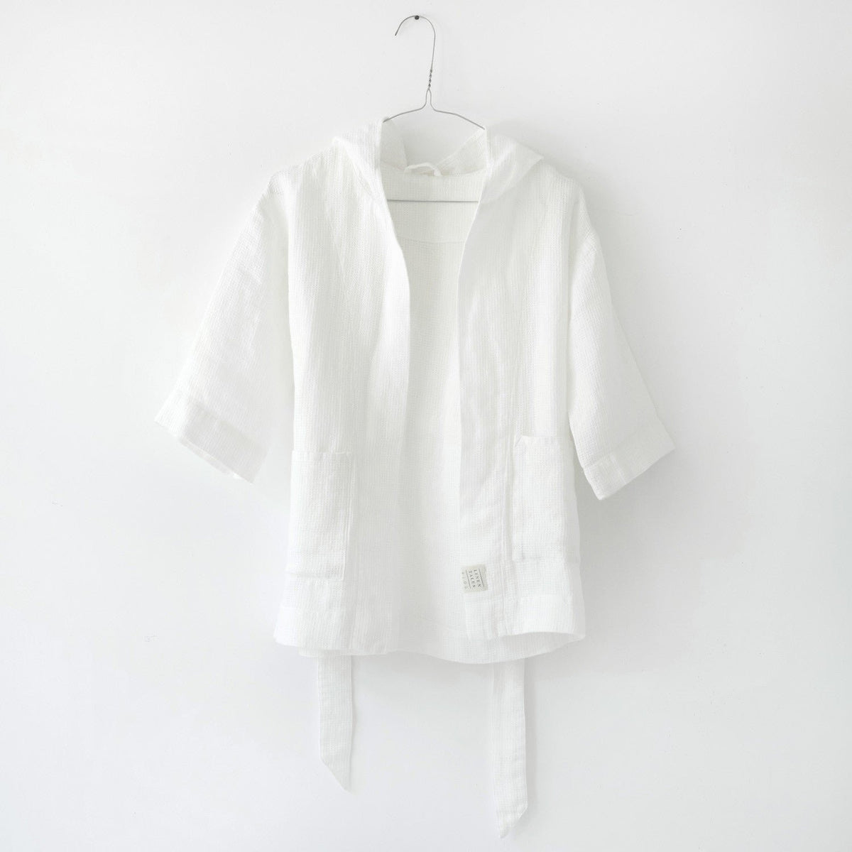 2. White linen bathrobe for kids with hood and belt, hanging on a hook against a white background