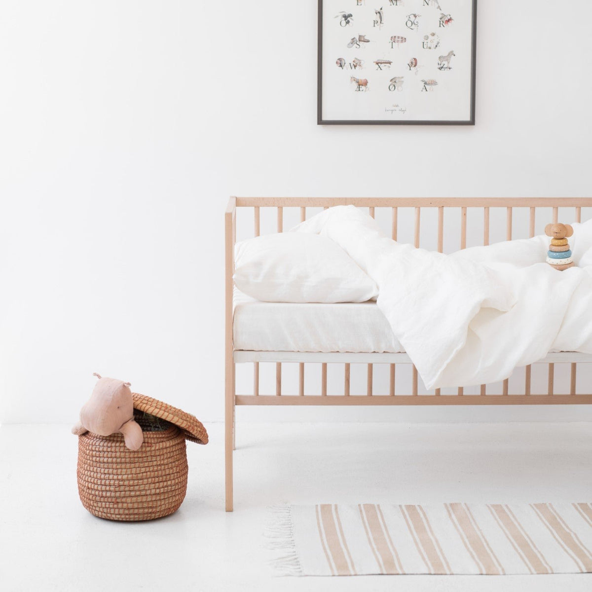 1. Kids' room with white linen duvet cover set on a crib, wicker basket, and wall art