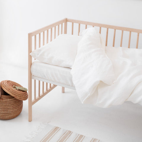 1. Wooden crib with white linen duvet cover set, wicker basket, and striped rug