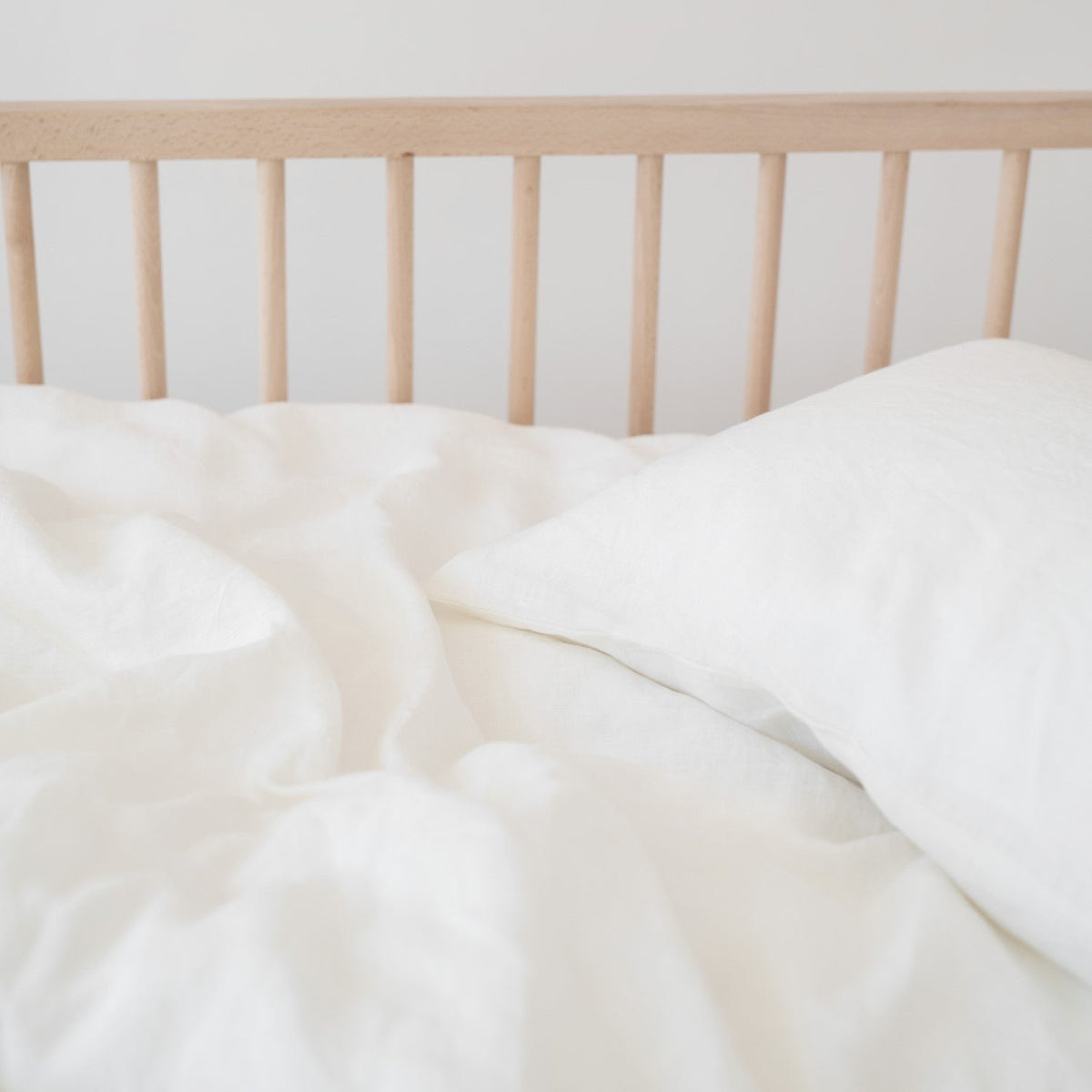 2. White linen duvet cover and pillow on a wooden crib, showcasing fabric texture