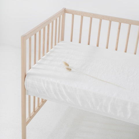 1. White linen fitted sheet on a wooden crib with a minimalistic design, showcasing the soft texture and elastic hem