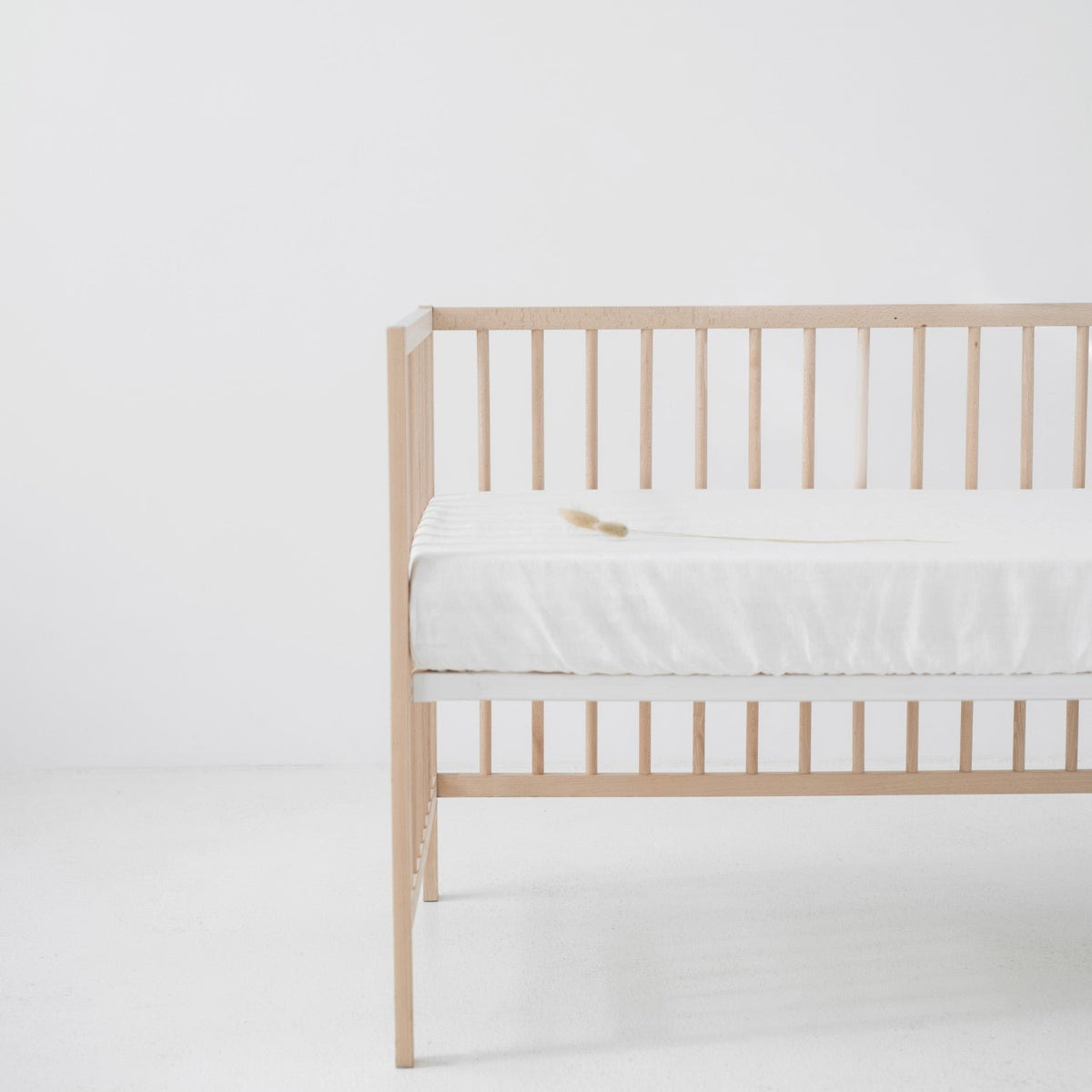 4. White linen fitted sheet on a wooden crib in a bright room, emphasizing the sheet's fit and texture