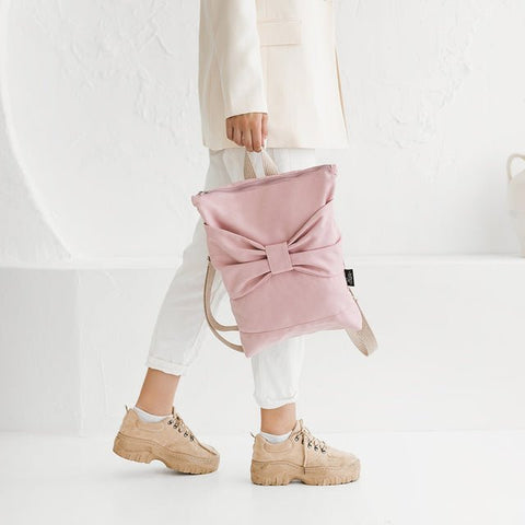 3. Woman carrying Muni Pink Bow backpack, styled with white outfit in lifestyle setting