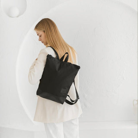 3. Woman in white outfit with Muni black leather backpack, emphasizing minimalist design and functionality
