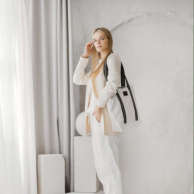 1. Woman wearing Muni white denim tote bag with black straps in a stylish indoor setting