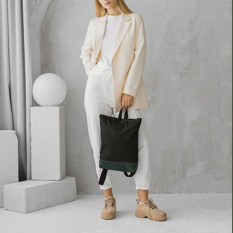 3. Woman holding Muni waterproof backpack with green leather bottom, styled with casual outfit in lifestyle setting