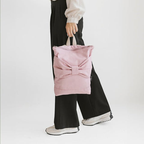 5. Woman holding Muni Pink Bow backpack, highlighting pink denim material