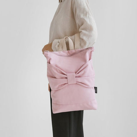 1. Woman holding Muni Pink Bow backpack in lifestyle setting, showcasing large bow detail