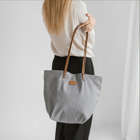 3. Woman holding Muni grey denim tote bag with tan leather handles, shown from the back in studio setting