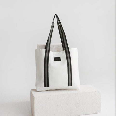 4. Studio shot of Muni white denim tote bag with black straps, displayed on a white block