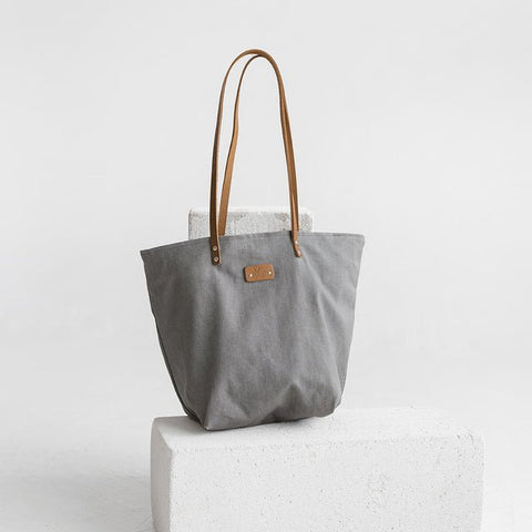 4. Studio shot of Muni grey denim tote bag with tan leather handles, displayed on white block