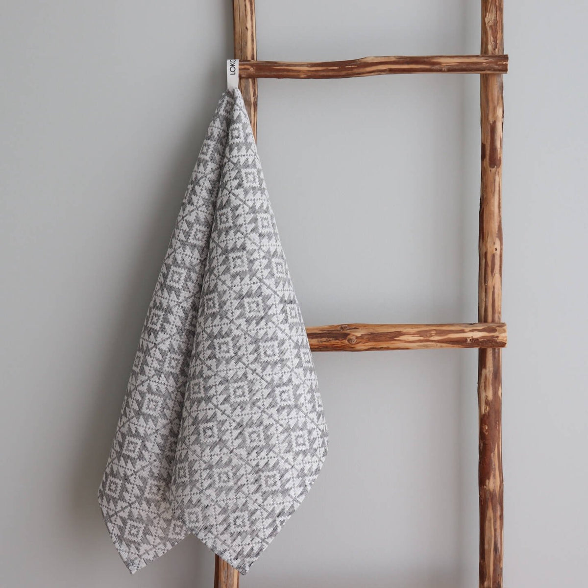 1. Grey kitchen towel with Harjumaa folk art pattern hanging on rustic wooden ladder, made of 52% linen and 48% cotton by LOKO, designed in Estonia
