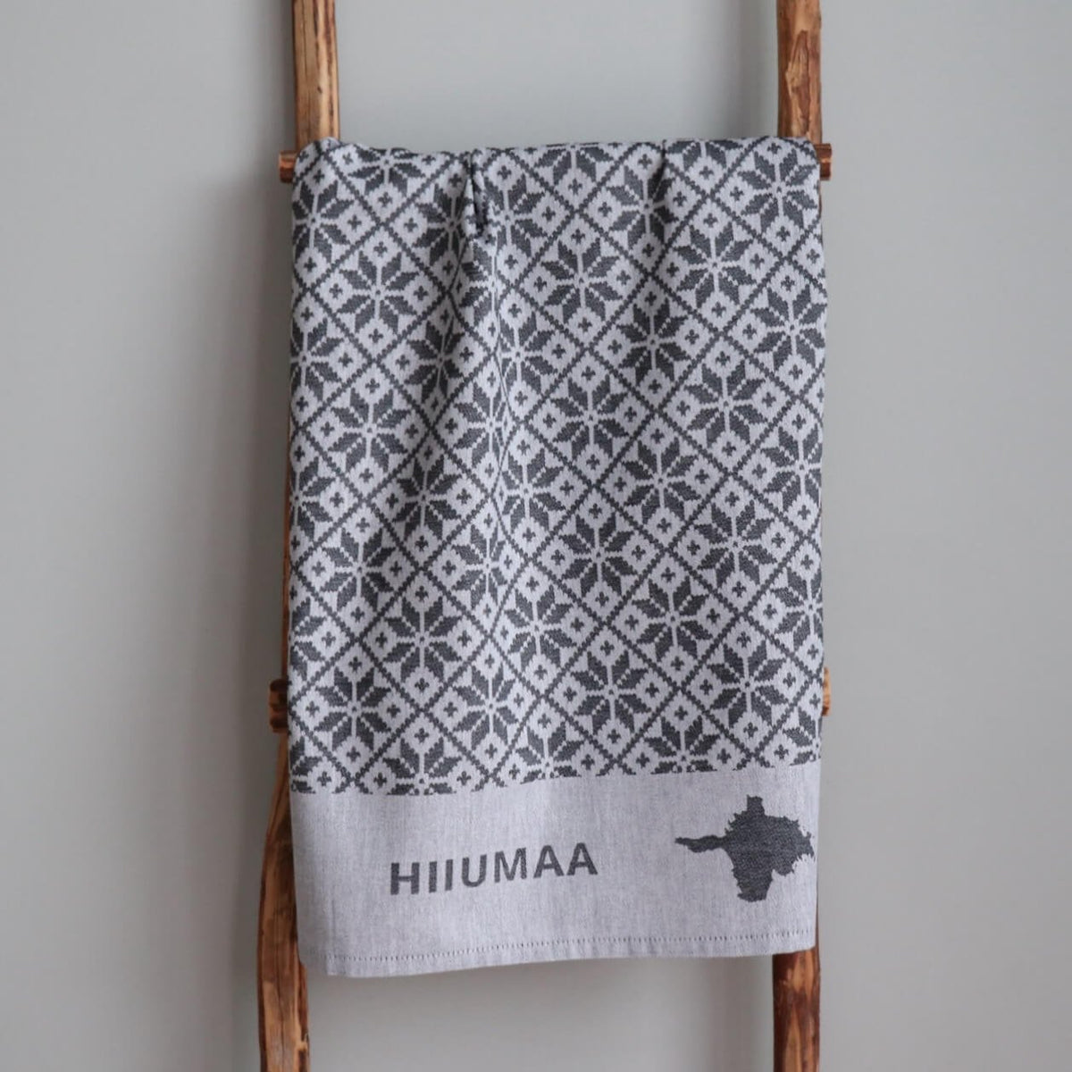 2. Grey kitchen towel with Pühalepa pattern, Hiiumaa text, and island outline hanging on ladder