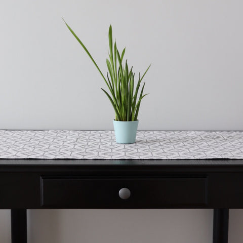 1. Table runner with Harjumaa folk art pattern in grey and white on dark wooden table with green plant in light blue pot
