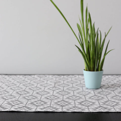 2. Close-up of grey and white Harjumaa pattern table runner with green plant in light blue pot on dark table