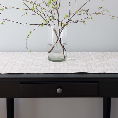 1. Beige table runner with kaheksakanna pattern on dark table, glass vase with branches, minimalist setting