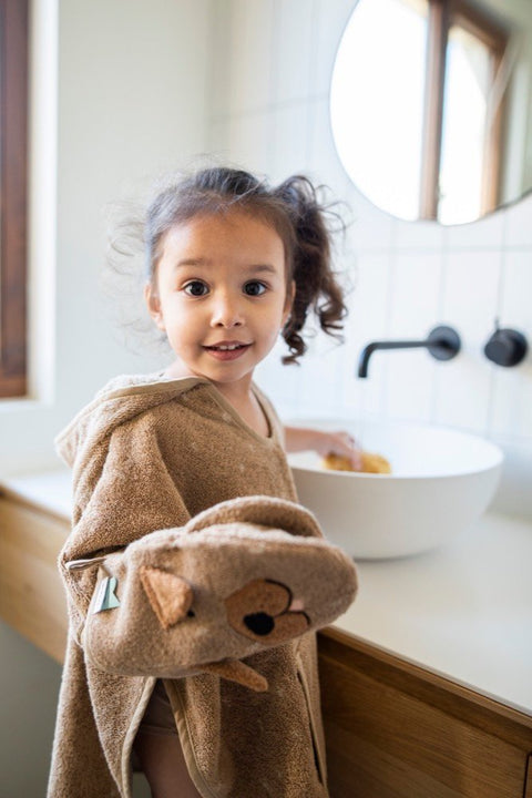 1. Smiling child wearing Trixie Baby Mr. Dog hooded poncho, standing by sink in bathroom