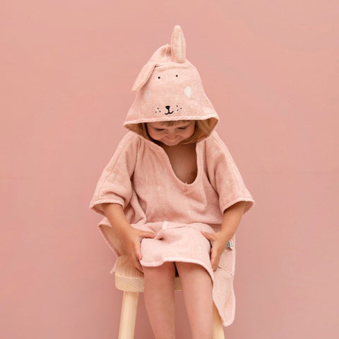 1. Child wearing pink hooded bathing poncho with rabbit design, sitting on stool against pink background