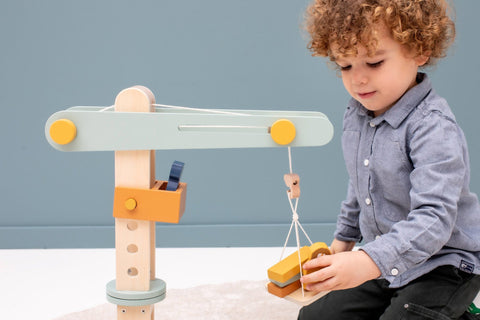 1. Child playing with Trixie Baby wooden construction crane featuring animal friends and building blocks in a playroom setting