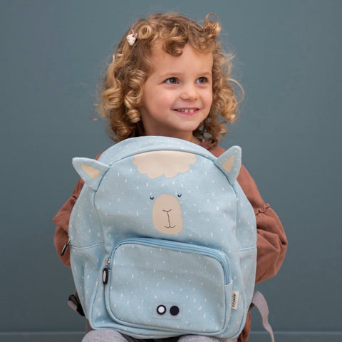 1. Child holding blue Mr Alpaca backpack with alpaca face design, smiling in front of a blue background