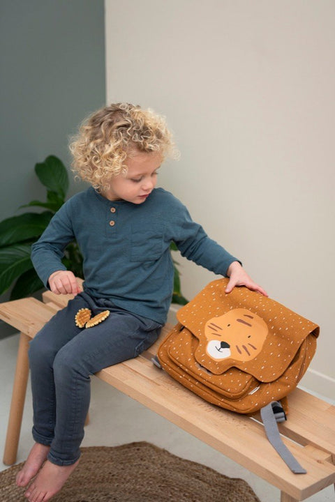 1. Child sitting on bench with Trixie Baby Mr Tiger school bag, showcasing playful design in a cozy indoor setting