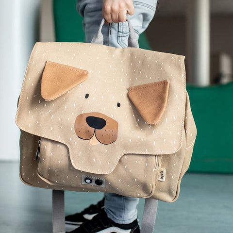 1. Child holding Trixie Baby Mr Dog school bag in beige with dog face design, indoor setting