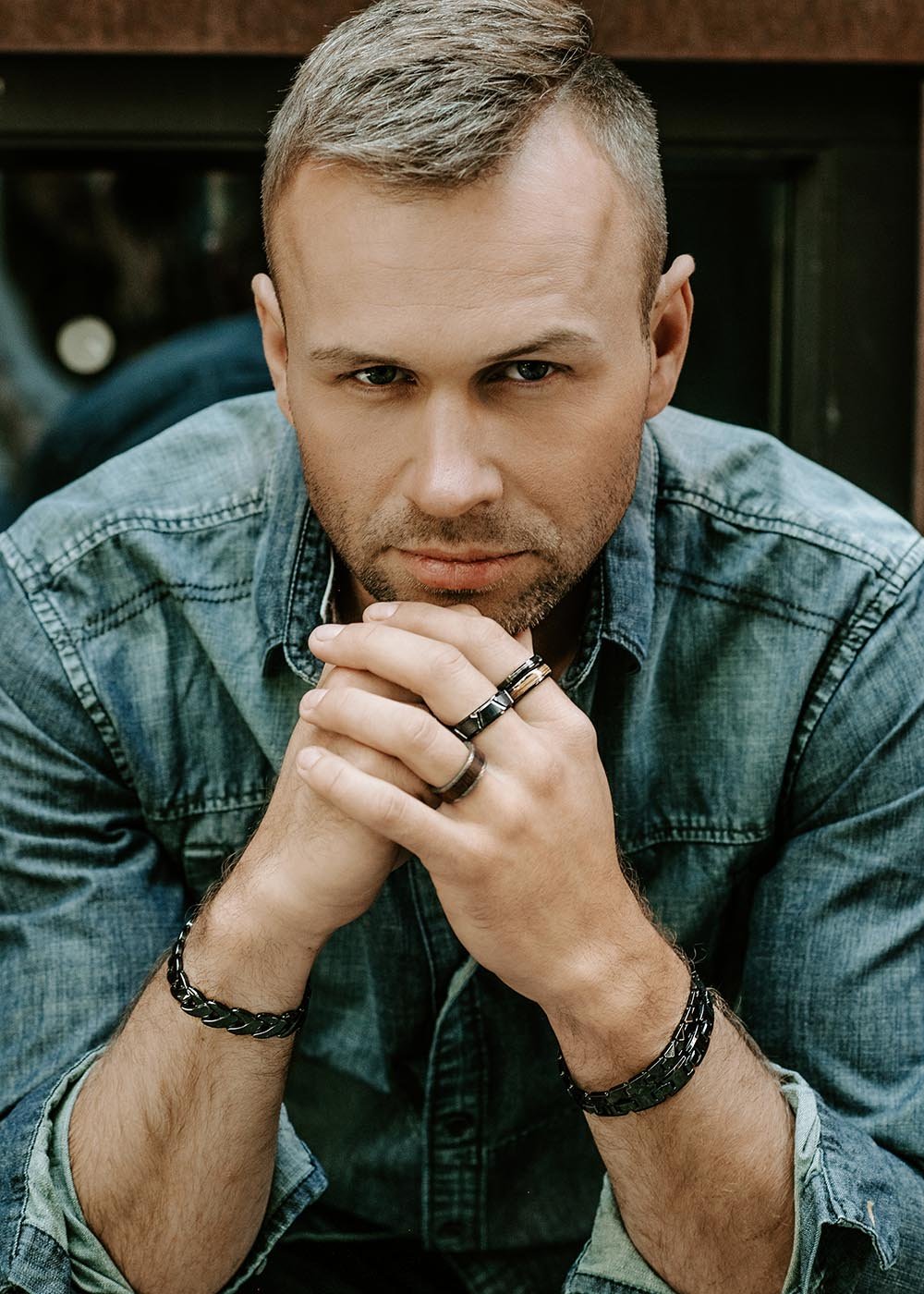 1. Man wearing Leomani men's Kahoy ring in black ceramic and natural veneer, styled with denim shirt, showcasing modern elegance