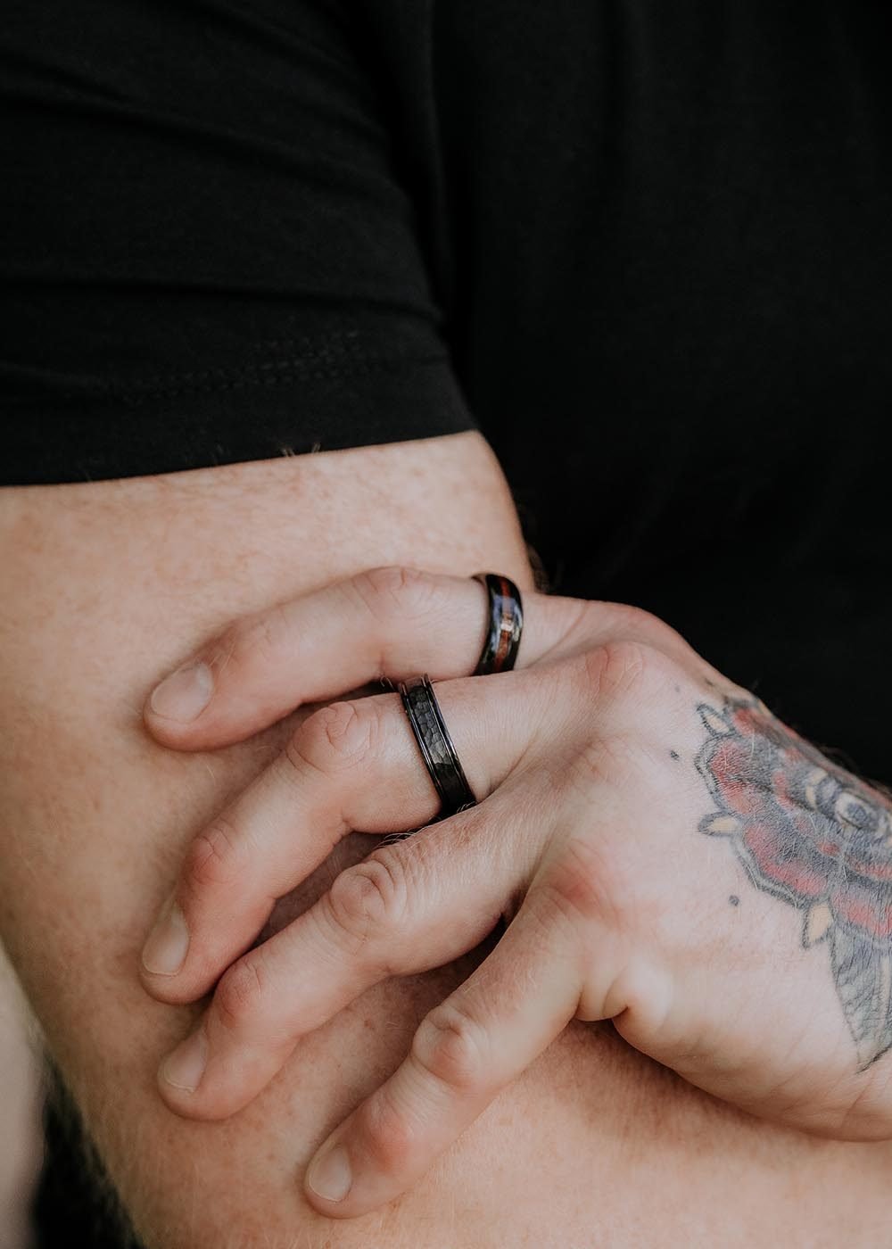 1. Man with tattooed hand wearing two black ceramic rings by Leomani, shown in a relaxed pose outdoors