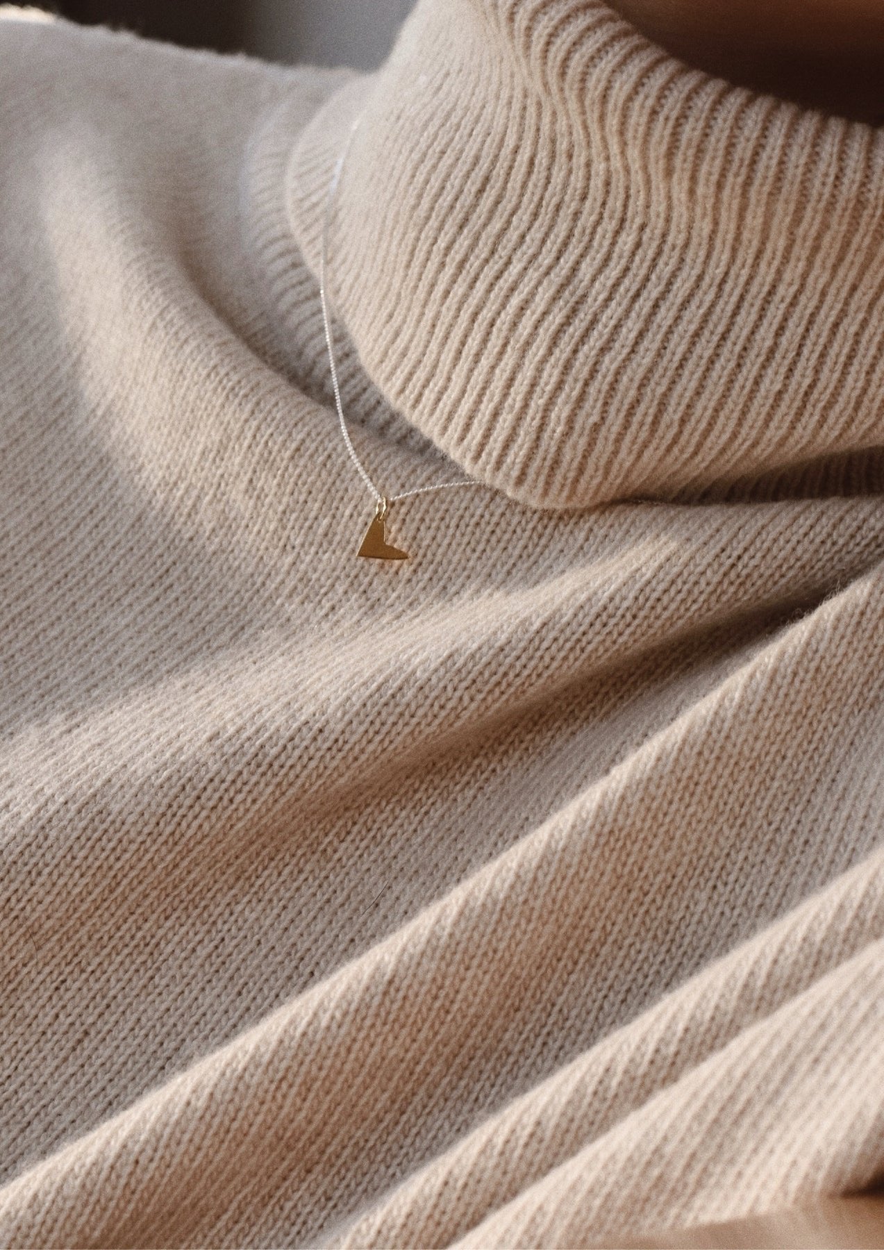 2. Love Necklace in gold by NO MORE, worn over a beige turtleneck sweater