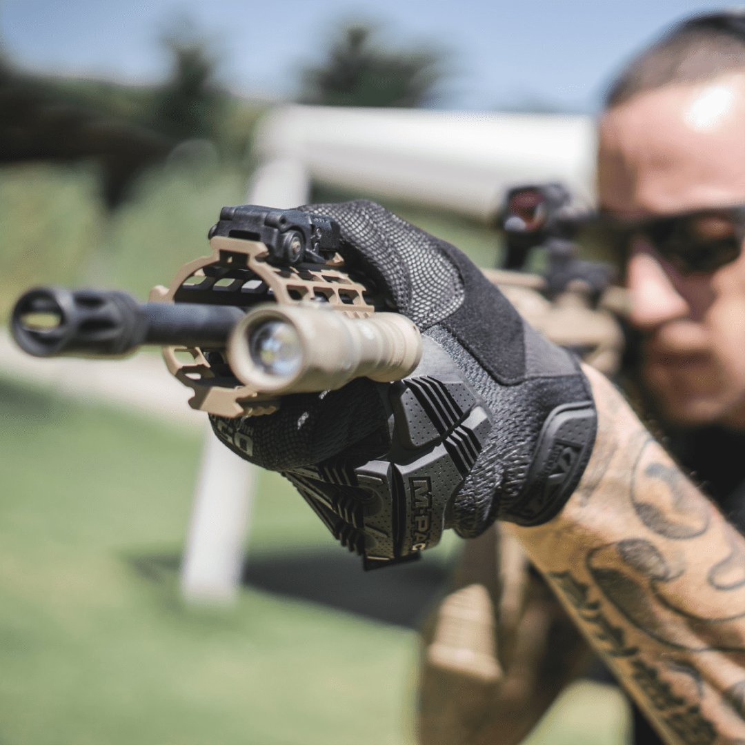 1. Person wearing black Mechanix M-Pact glove aiming a rifle outdoors