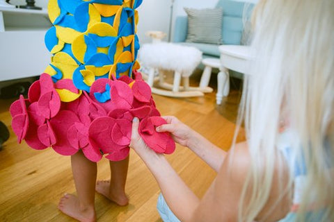 2. Child assembling pink felt pieces onto a colorful costume in a living room setting