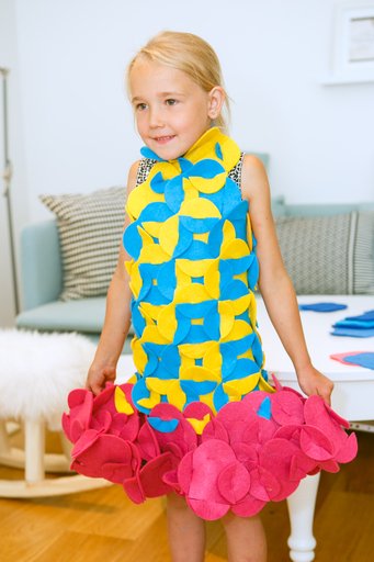 4. Young girl wearing a blue and yellow felt costume with pink accents, smiling indoors