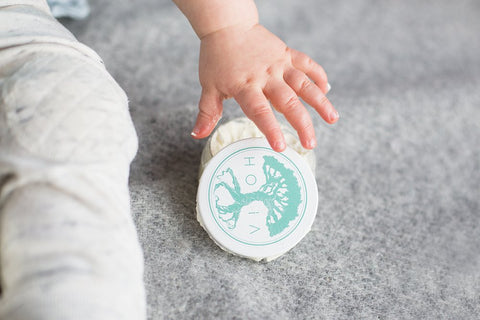 1. Baby's hand reaching for HOIA homespa Baby Cream jar on soft surface, highlighting gentle care for sensitive skin