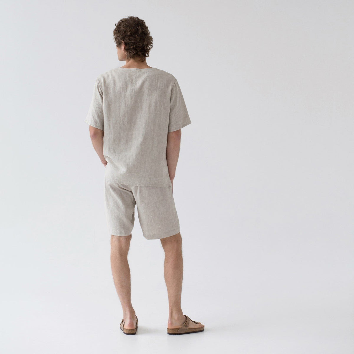 2. Back view of men's beige linen pyjama set with short sleeves and shorts, shown in studio setting