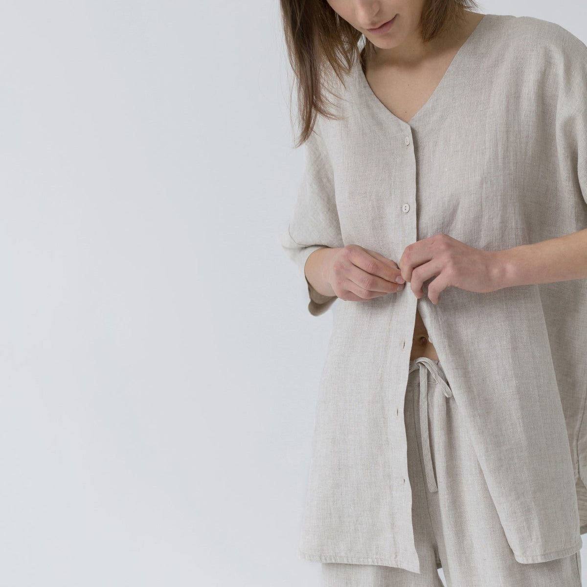 3. Close-up of woman buttoning melange linen loungewear top with drawstring pants
