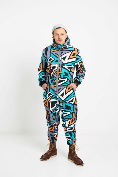 1. Man wearing Nuckö TANIEL softshell overall with geometric print in blue, orange, and grey, standing in studio setting