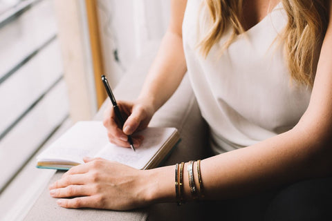 3. Woman writing while wearing Olla RAKAS ĆITI bracelet, highlighting its stylish and versatile design