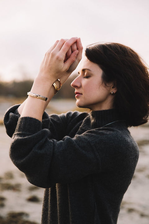 4. Woman meditating on the beach wearing Olla VHENGITĆ NAUTI OLE bracelets in silver, rose gold, and gold