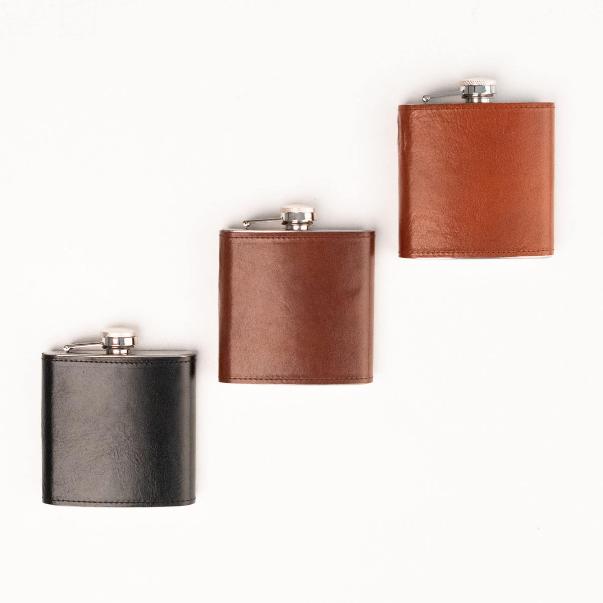 2. Flat lay of Papillon Hip Flask No. 21 in black, brown, and tan leather with stainless steel caps