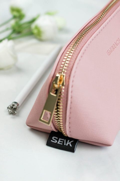4. Close-up of SEIK pink pencil case with gold zipper and embossed phrase, styled with flowers