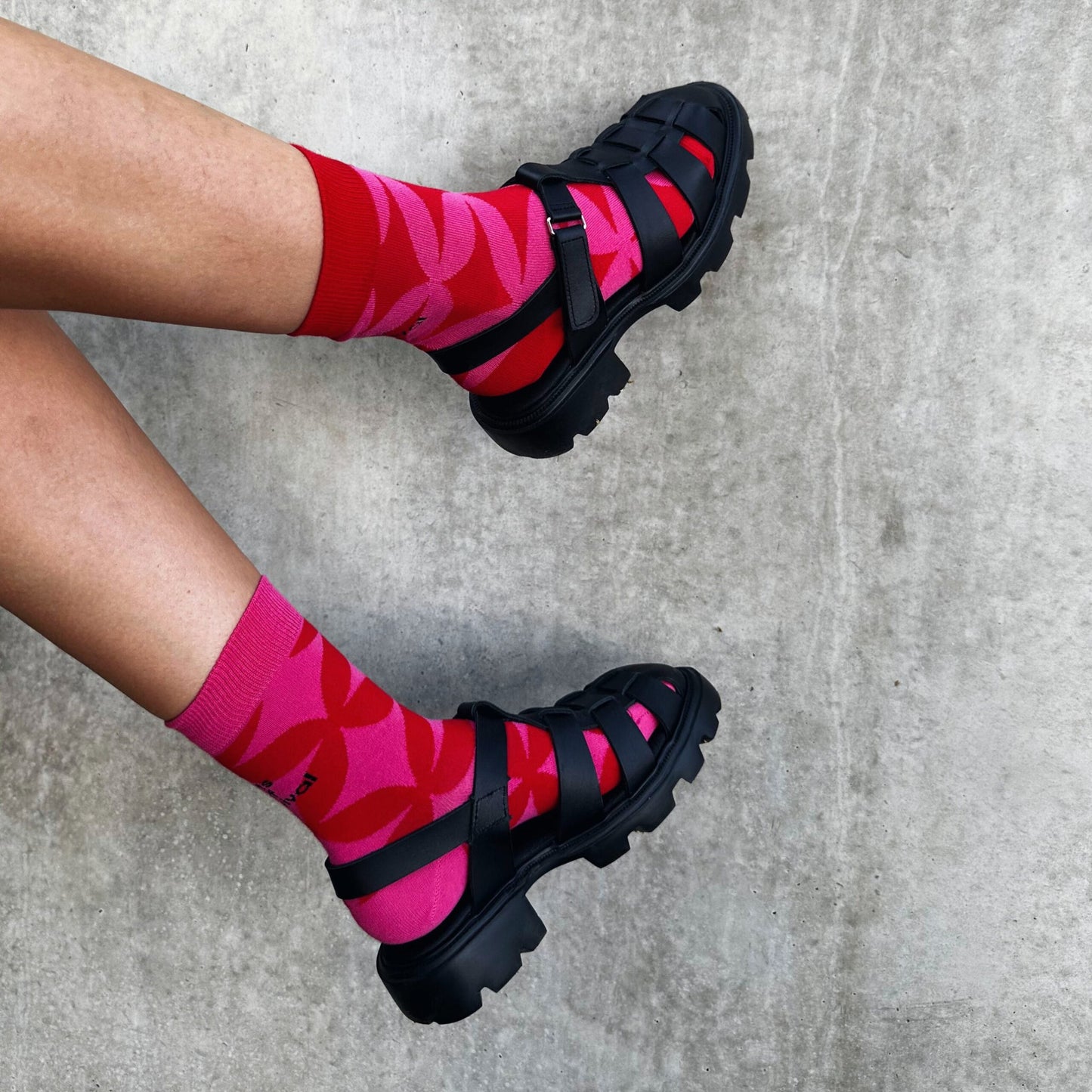 11. Women's black Samelin sandals with red socks, shown from side on concrete
