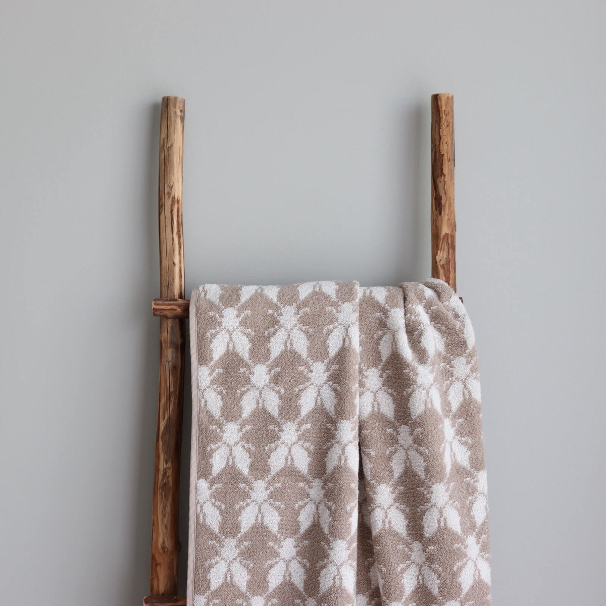 1. Beige and white terry sauna towel with Hiiumaa County mitten pattern draped over a rustic wooden ladder against a grey wall