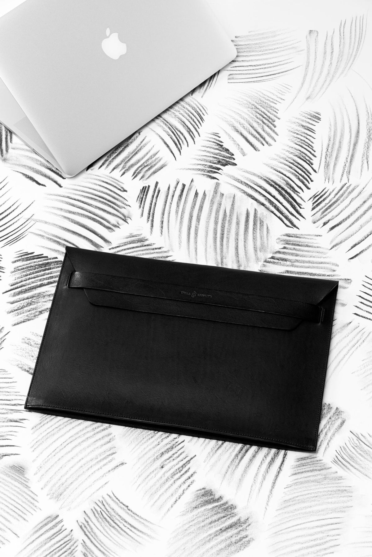 2. Black Stella Soomlais leather laptop sleeve with flap on patterned surface next to an open laptop