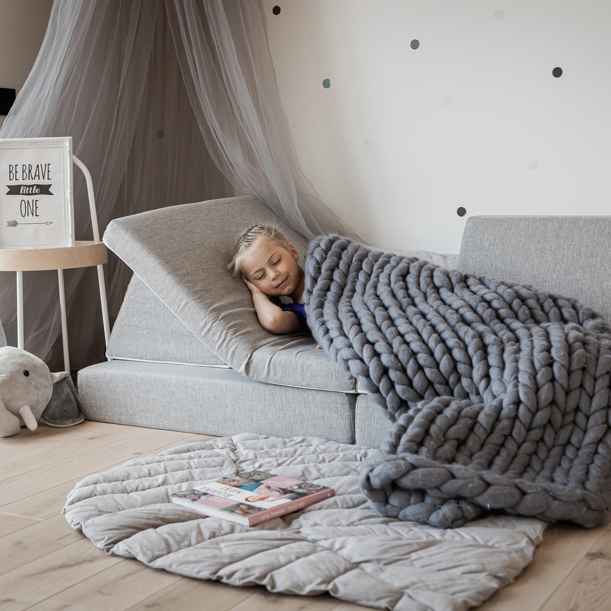 1. Child sleeping on grey Monboxy activity play mattress set with knitted blanket in cozy room