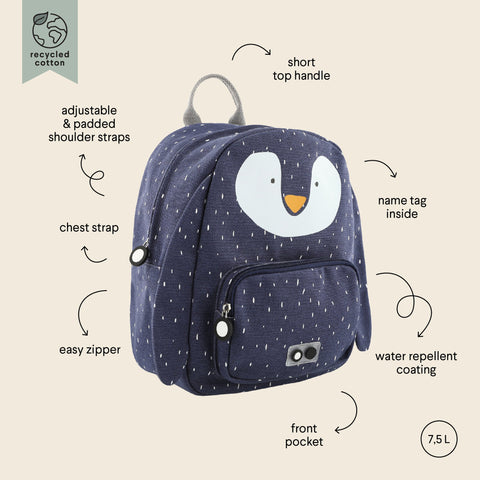 1. Navy blue Mr Penguin backpack with white penguin face, adjustable padded shoulder straps, chest strap, and front pocket, shown with labeled features on beige background