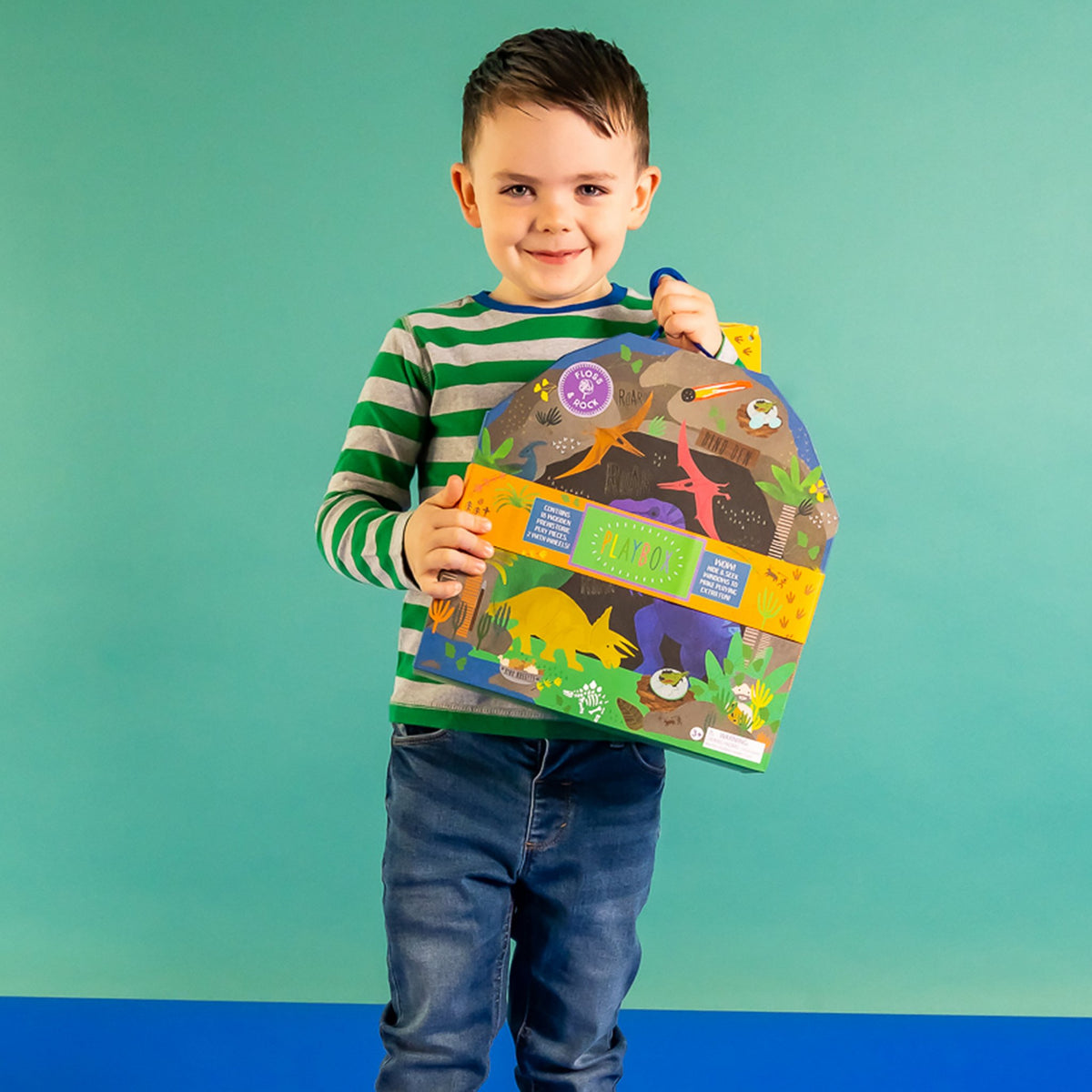 5. Young boy holding dinosaur play box with colorful design against a green background