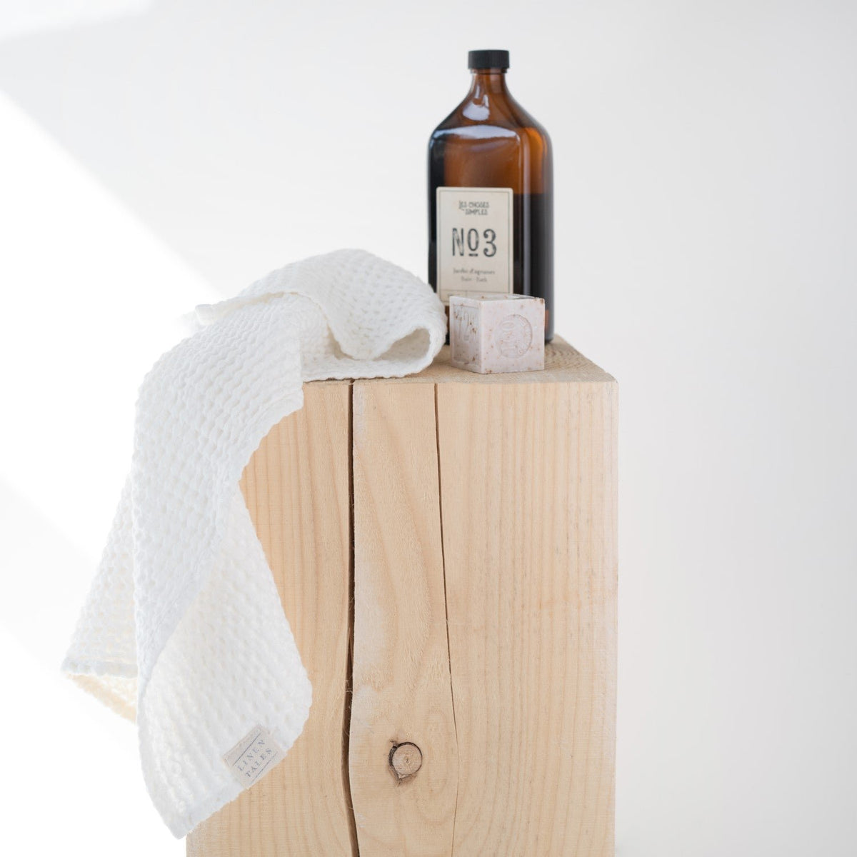 1. White honeycomb waffle towel draped over wooden block with amber bottle, highlighting texture
