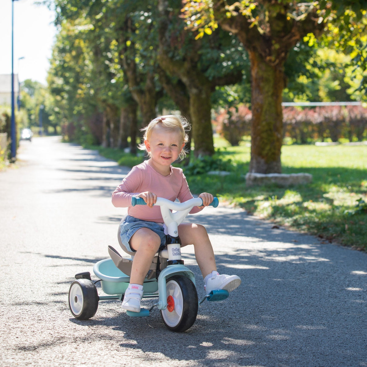 1. Child riding a blue Smoby Baby Balade Plus tricycle on a sunny path