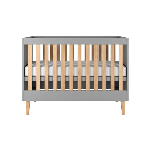 2. Front view of grey baby cot with oak slats and legs in studio setting, showcasing modern design