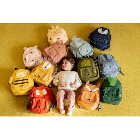 2. Child lying on yellow carpet surrounded by colorful animal-themed backpacks including Mr. Bumblebee